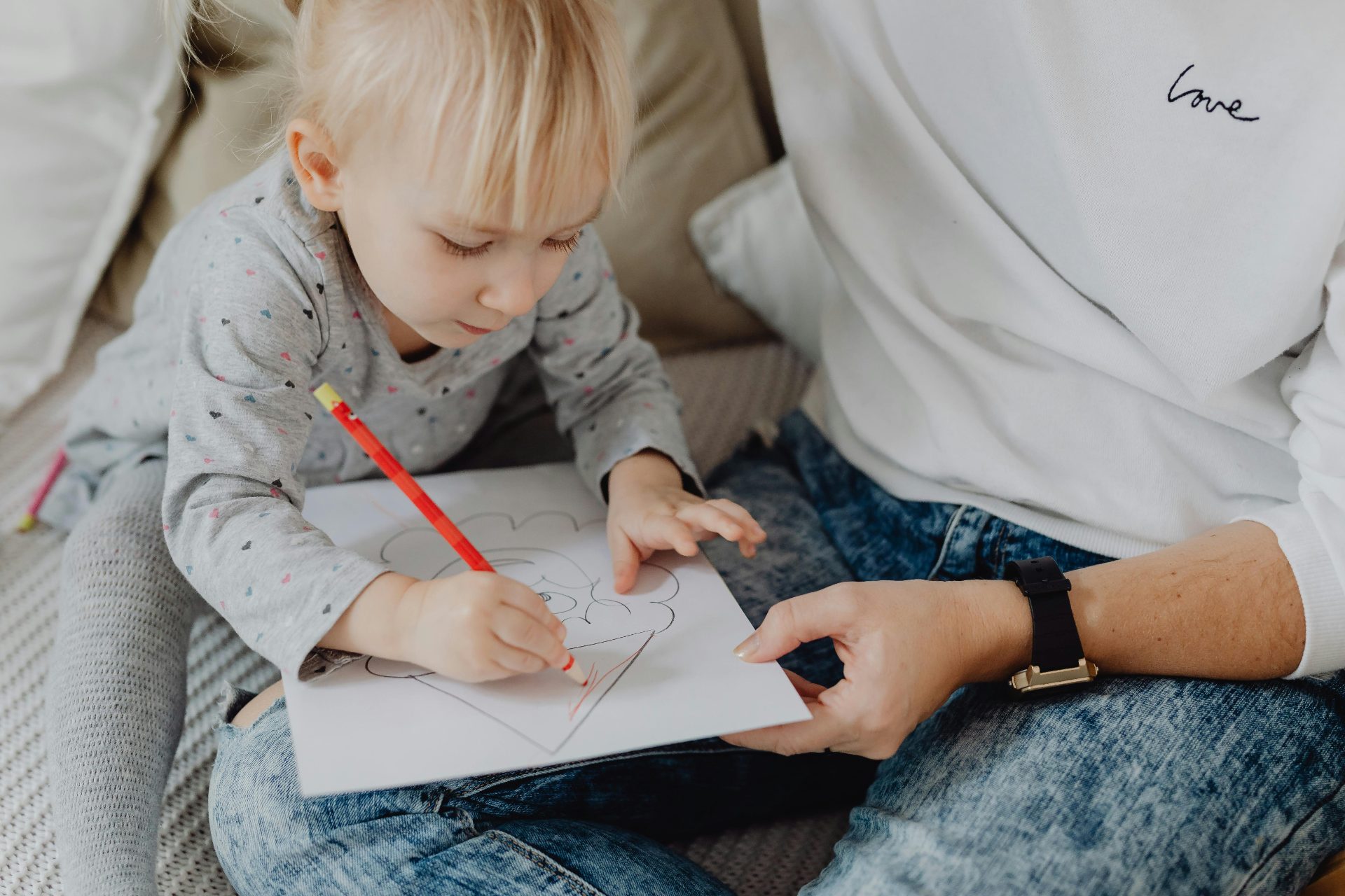 Primo piano di un bambino che colora un disegno mentre è seduto sulle ginocchia di un adulto.