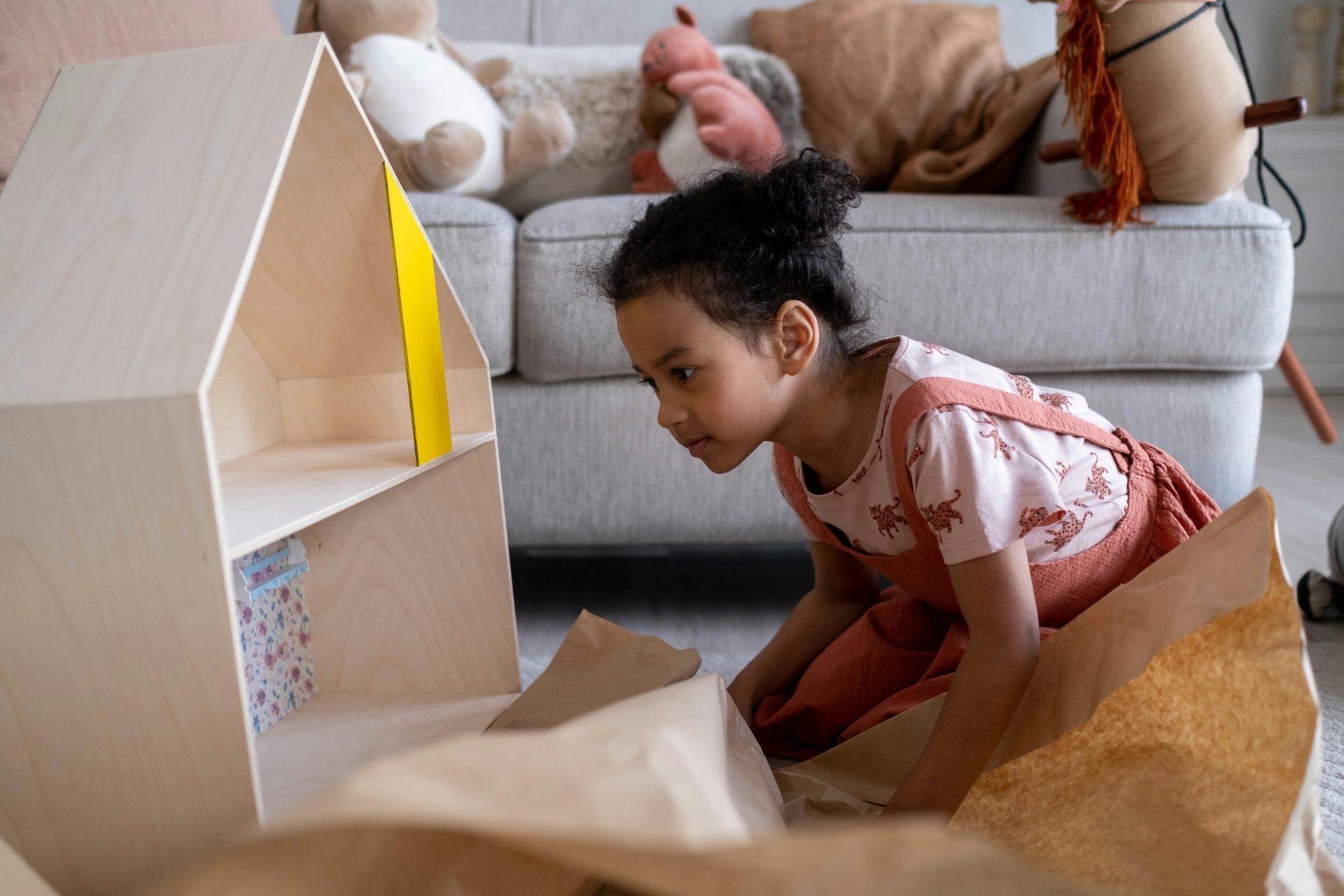 Una bambina è seduta sul pavimento mentre gioca con una casa delle bambole di legno.